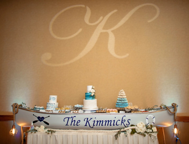 A wedding dessert table in a boat setup with cakes and treats, decorated with flowers and nautical decor, featuring a large 