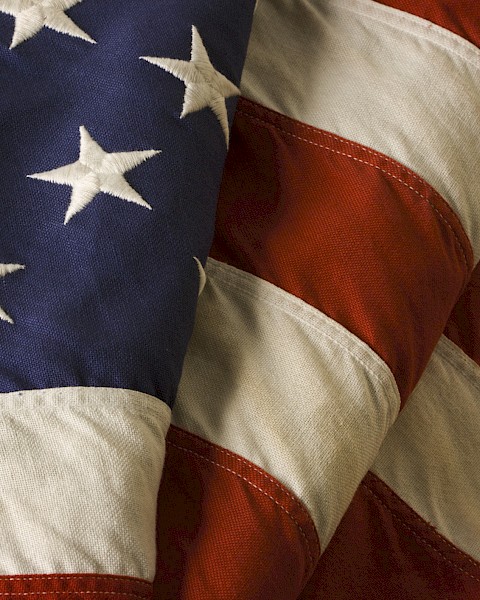 The image shows a close-up of the United States flag, displaying stars on a blue field and red and white stripes.