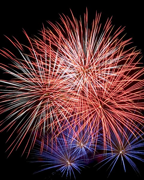 Fireworks explode in the night sky, displaying vibrant red and blue bursts.