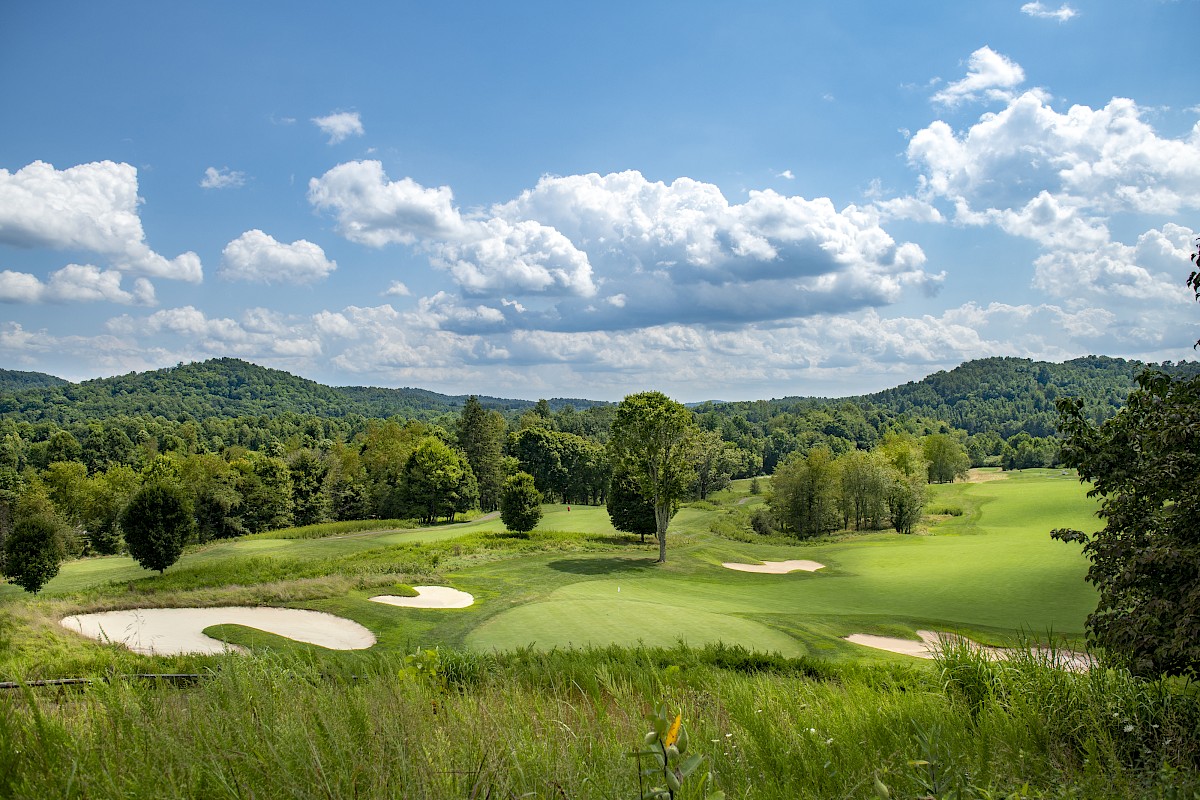 A scenic golf course with rolling hills, sand traps, and lush greenery under a blue sky with clouds.