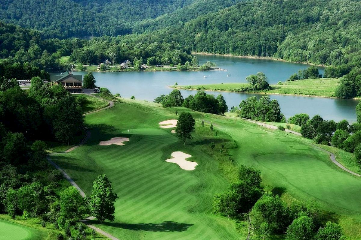 This image shows a scenic view of a golf course with well-manicured greens, sand bunkers, surrounded by a lush forest and a serene lake in the background.