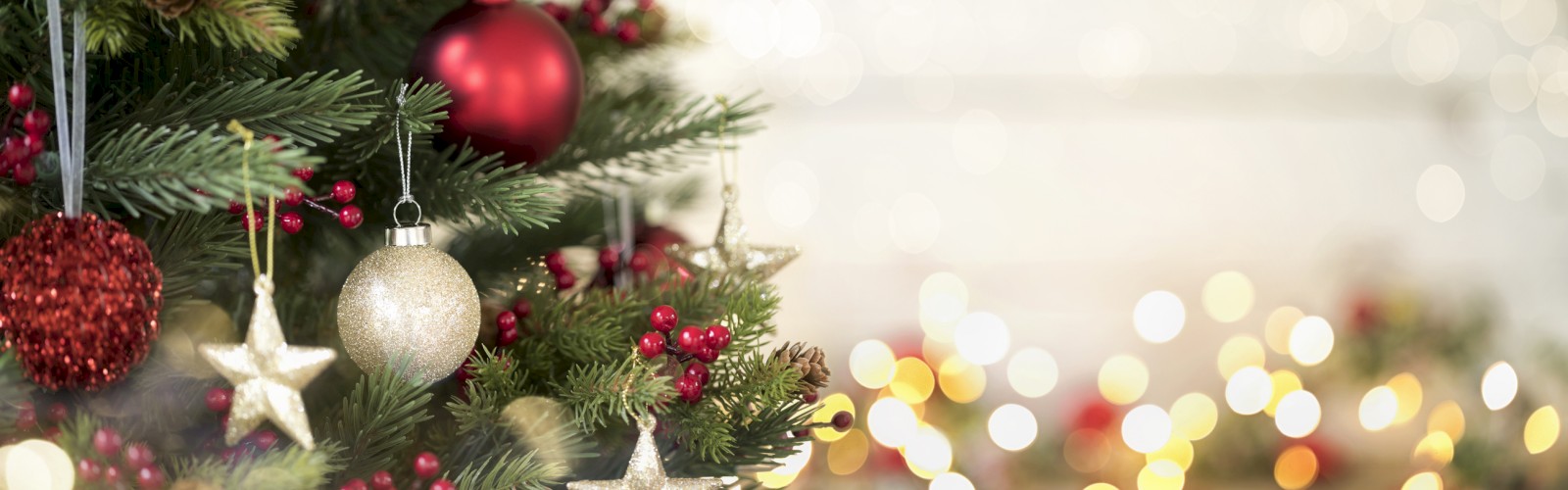 A decorated Christmas tree with red and gold baubles, stars, red berries, and warm bokeh lights in the background, festive and cozy.