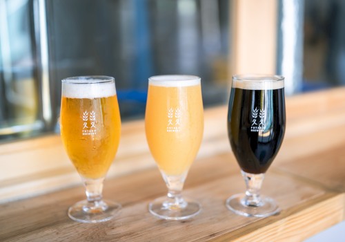 Three glasses of beer in varying shades from light to dark on a wooden surface, with a blurred background.