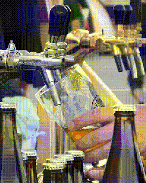 A person is pouring beer from a tap into a glass, surrounded by bottles and cups at an outdoor setting with multiple taps visible.