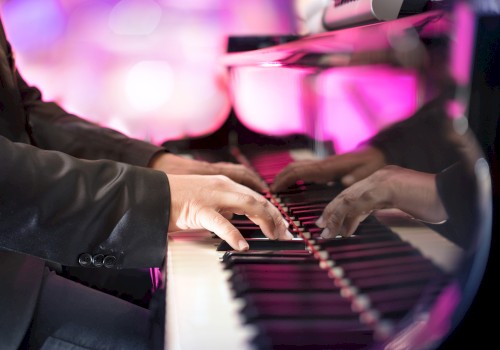 A person in a suit playing a grand piano, with vibrant pink and purple lighting reflecting off the polished surface.