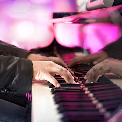 A person in a suit playing a grand piano, with vibrant pink and purple lighting reflecting off the polished surface.