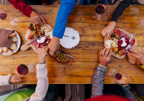 A group of people sharing charcuterie boards and wine at a wooden table, with various meats, cheeses, and bread.