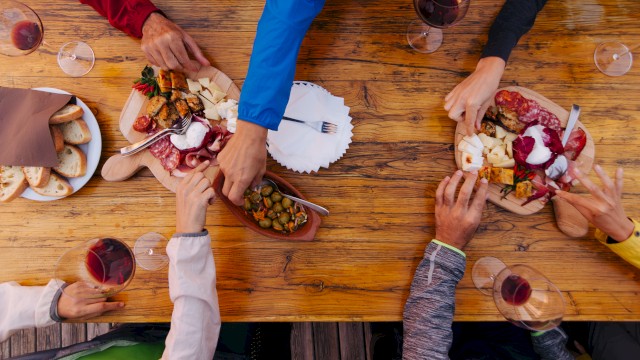 A group of people sharing charcuterie boards and wine at a wooden table, with various meats, cheeses, and bread.
