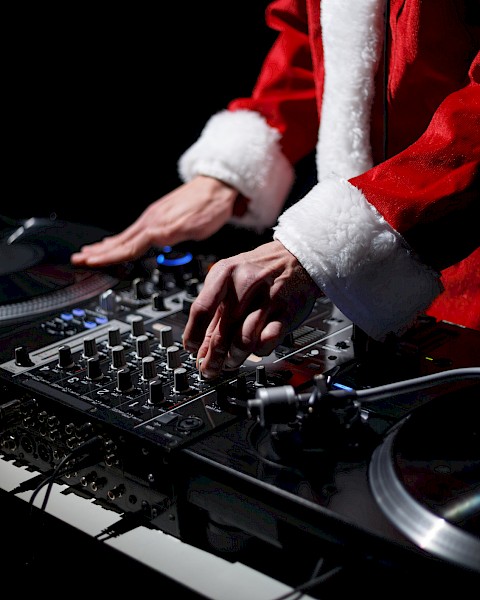 A person dressed in a Santa suit is DJing, using a mixer and turntables.
