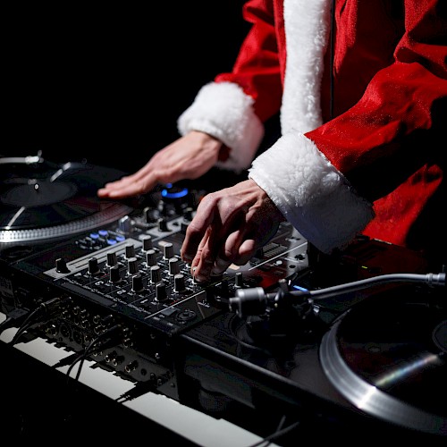 A person dressed in a Santa suit is DJing, using a mixer and turntables.