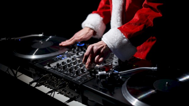 A person dressed in a Santa suit is DJing, using a mixer and turntables.