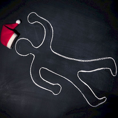 A chalk outline of a person on a dark surface with a Santa hat placed near the head of the outline, suggesting a playful holiday theme.