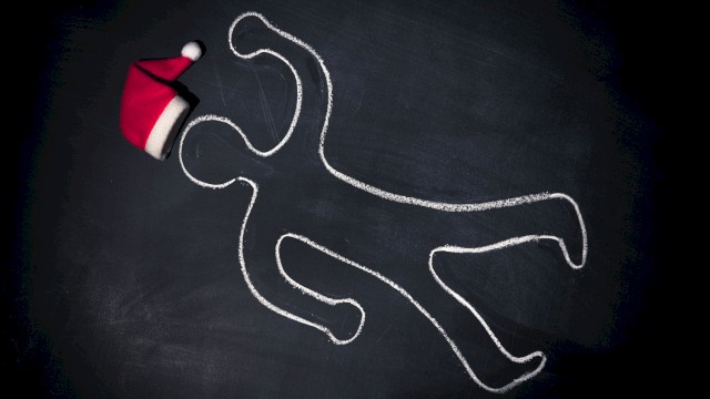 A chalk outline of a person on a dark surface with a Santa hat placed near the head of the outline, suggesting a playful holiday theme.