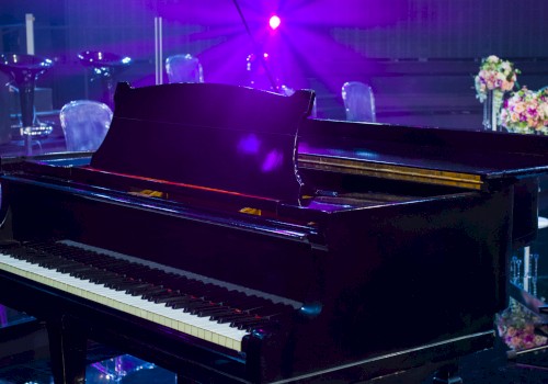 A grand piano on a stage with purple lighting and floral decorations in the background.