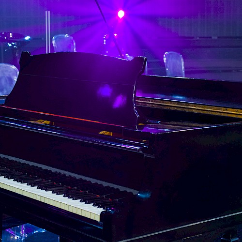 A grand piano on a stage with purple lighting and floral decorations in the background.