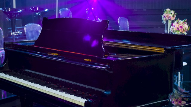 A grand piano on a stage with purple lighting and floral decorations in the background.