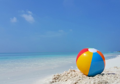 A colorful beach ball on pristine sand against a serene ocean backdrop under a clear blue sky.