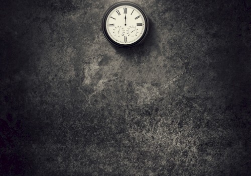 A dimly lit room with a hanging lightbulb and a wall clock showing 10:10, casting shadows on a textured wall.