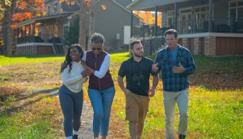A diverse group of four friends walk and talk together on a sunny autumn day in a residential neighborhood.