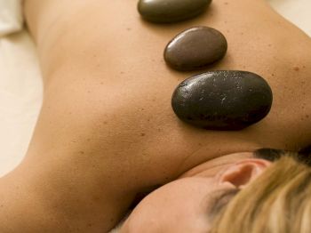 A person lying face down with hot stones placed along their back for a spa treatment, covered with a towel.